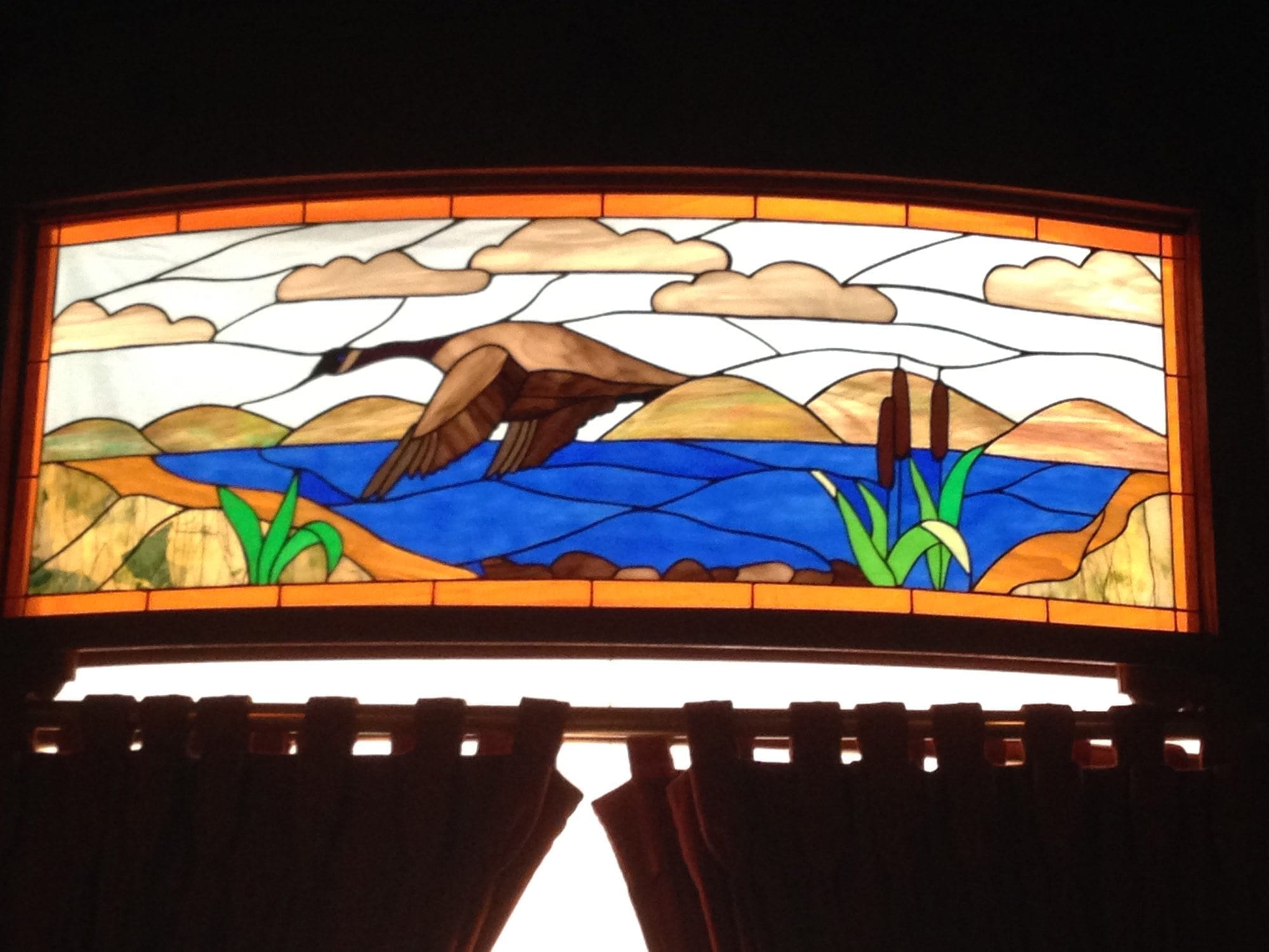 Stained glass depicting a Canadian goose flying over a lake